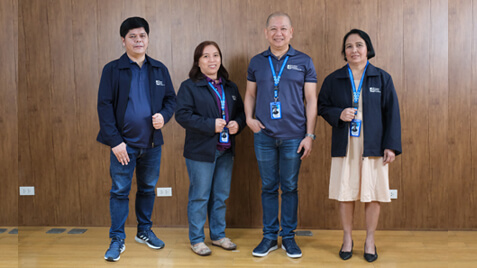 Four finance employees stand side-by-side against a wooden wall, smiling for the camera.