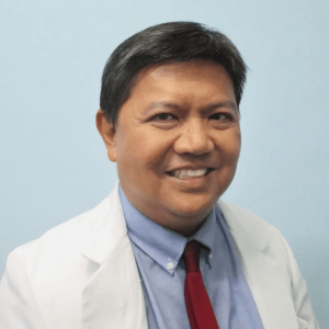 Professional studio headshot of Dr. Ruben Encarnacion smiling gently. He is wearing a formal white medical coat over a dark collared shirt and red necktie, against a light backdrop.